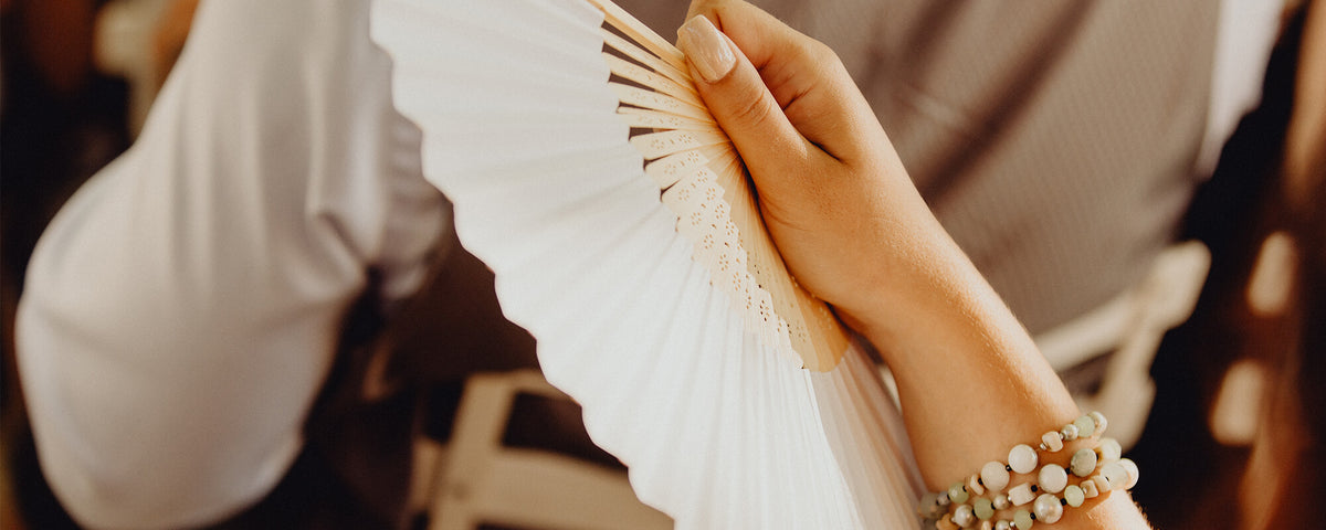 Invités de mariage tenant des éventails blancs en tissu et bambou